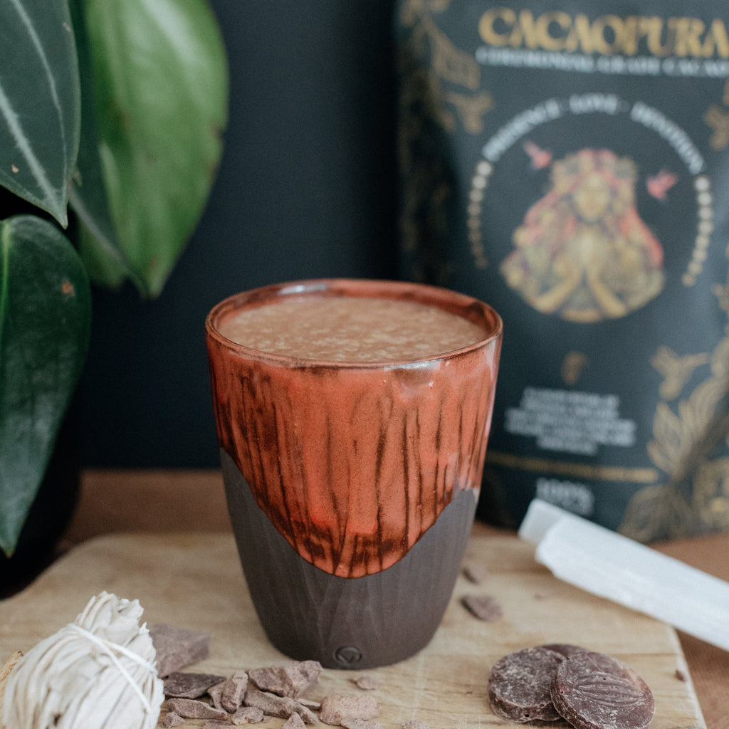 Ceramic mug with a dark brown interior on a wooden board with Cacao Pura packaging in the background.