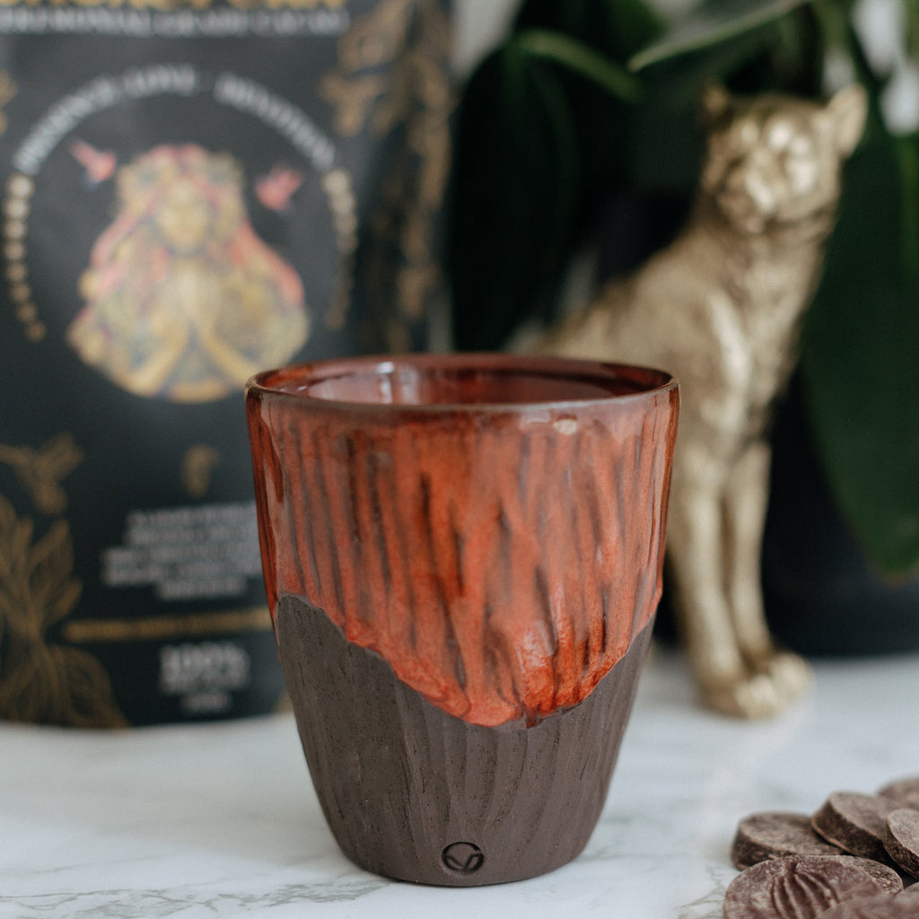 Ceremonial cacao cup, cacao vessel. Brown and red ceramic cup on a marble surface with a Cacaopura bag  in the background.
